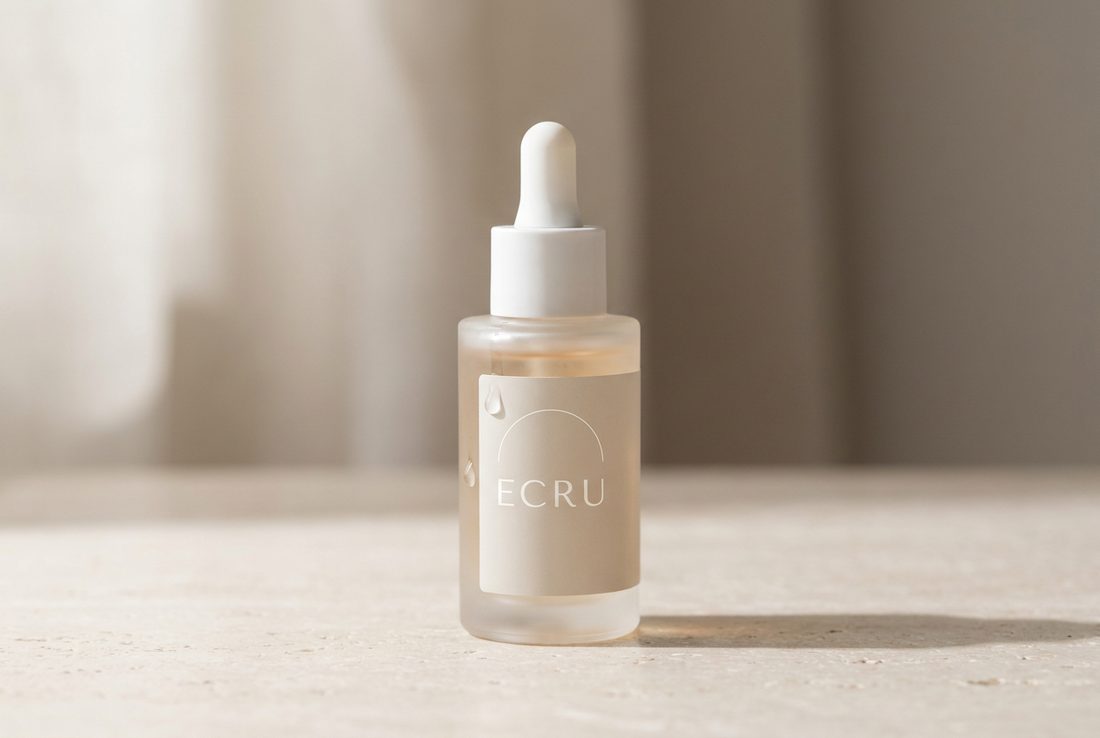 ECRU serum bottle photographed with restrained reflections on a pale stone surface